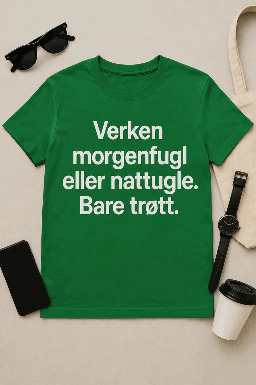 Grønn morsom t-skjorte med hvit tekst om morgenfugl og nattugle, lagt flatt med kaffe og mobil