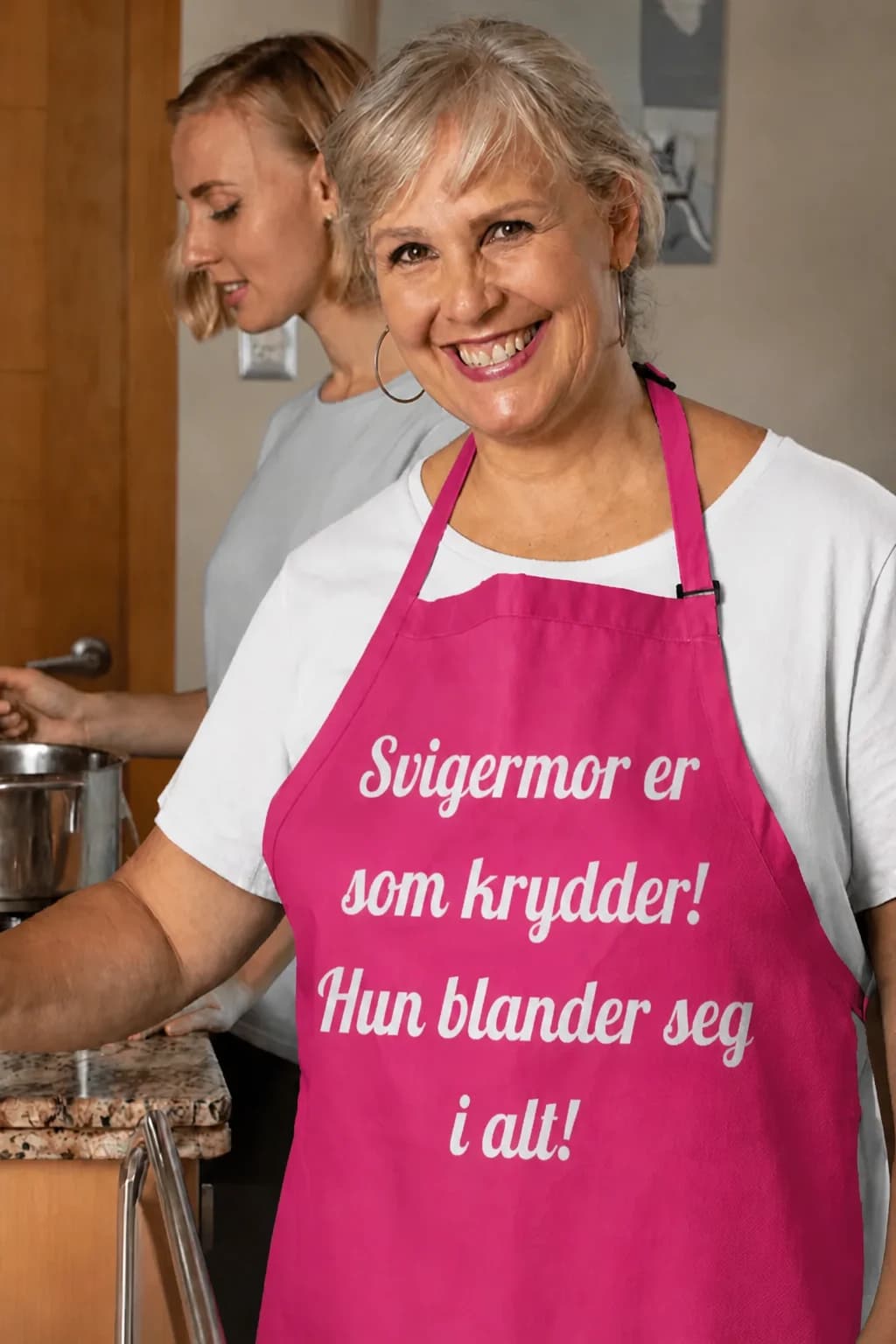 Rosa forkle til svigermor med hvit tekst «Svigermor er som krydder! Hun blander seg i alt!»