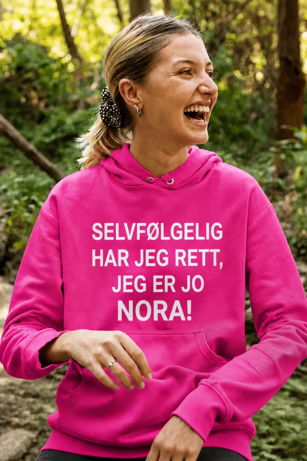 Leende kvinne i rosa hettegenser med tekst «SELVFØLGELIG HAR JEG RETT, JEG ER JO NORA!» med navn