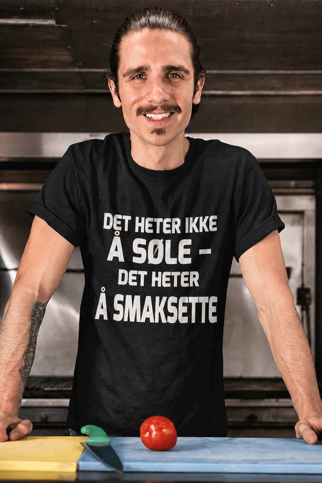 Mann på kjøkkenet i svart morsom t-skjorte til kokken med tekst om å søle og smaksette