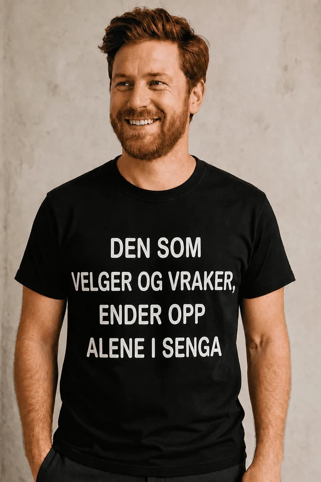 Smilende mann i svart morsom t-skjorte med teksten «Den som velger og vraker ender opp alene i senga»