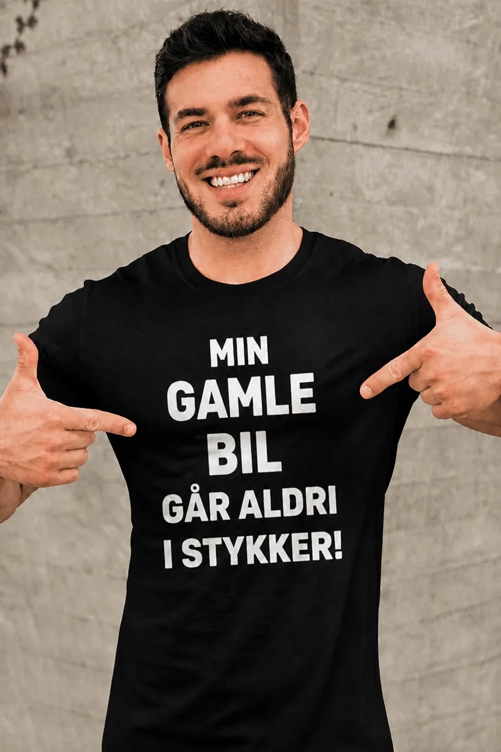 Svart t-skjorte med hvit tekst «Min gamle bil går aldri i stykker!» på en smilende mann, morsom t-skjorte til bilentusiast