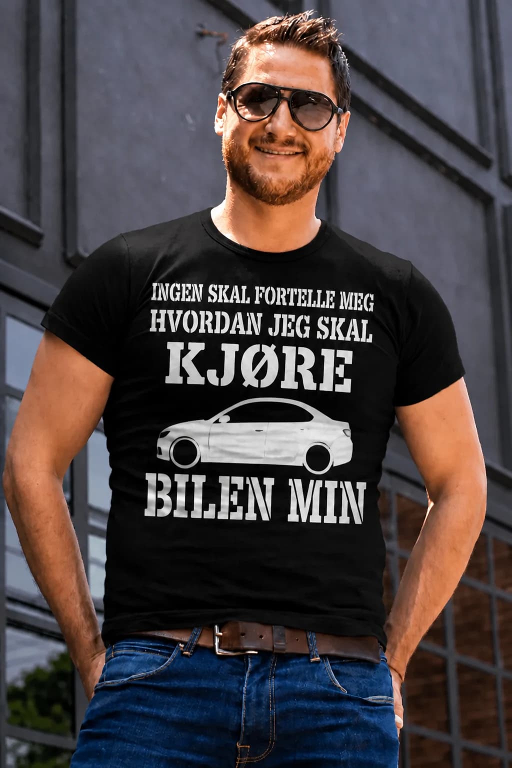 Svart bil-t-skjorte med hvit tekst om at ingen skal fortelle ham hvordan han skal kjøre, og tegning av en bil