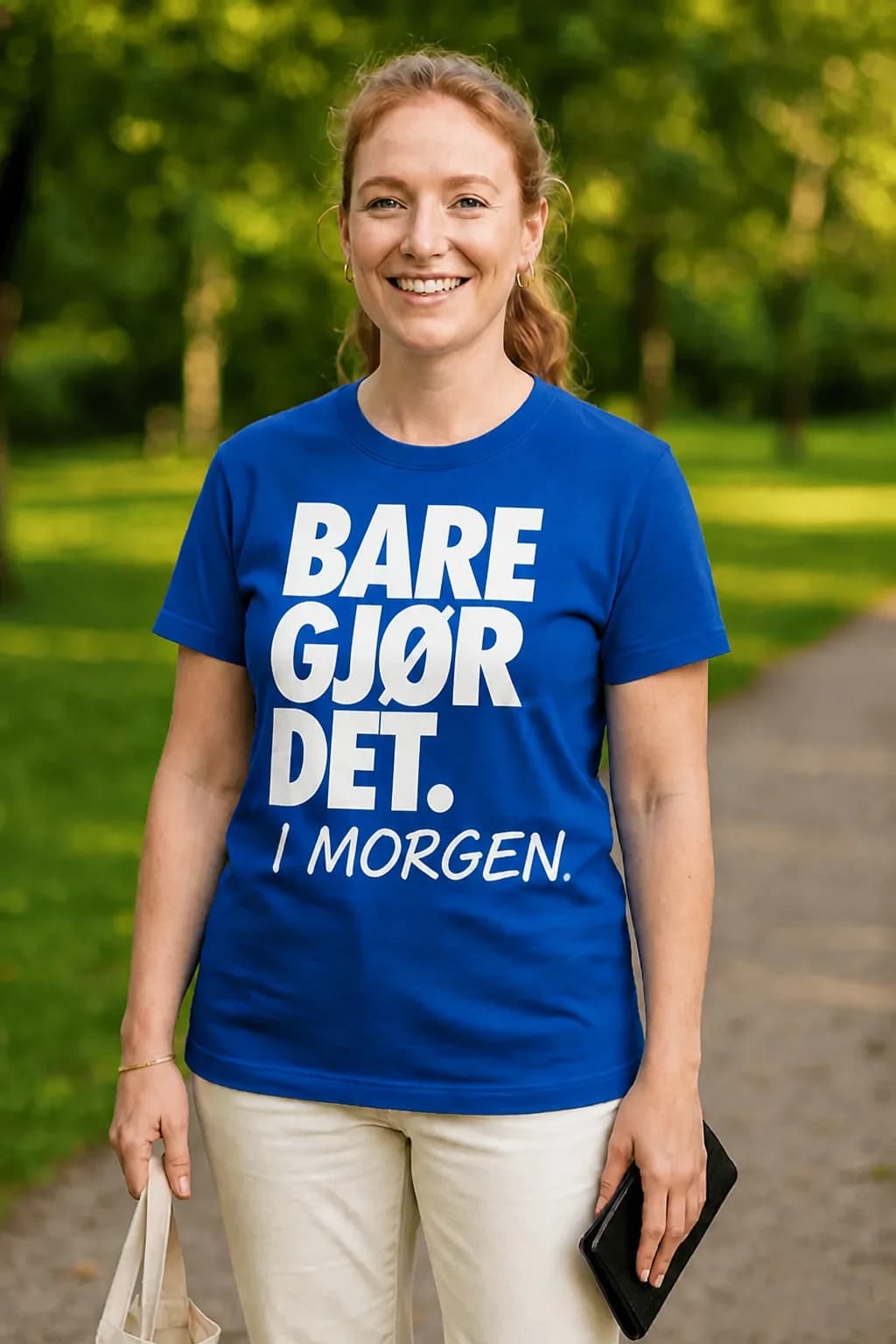 Smilende kvinne i kongeblå morsom t-skjorte med hvit tekst «Bare gjør det» og håndskrevet «i morgen»
