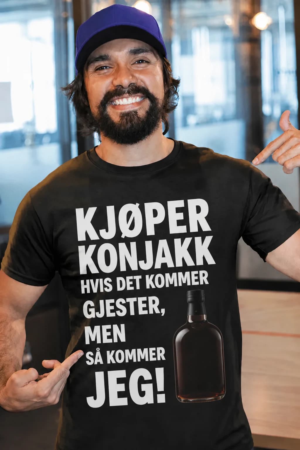 Smilende skjeggete mann i svart morsom t-skjorte med hvit tekst om å kjøpe konjakk til gjestene og en flaske