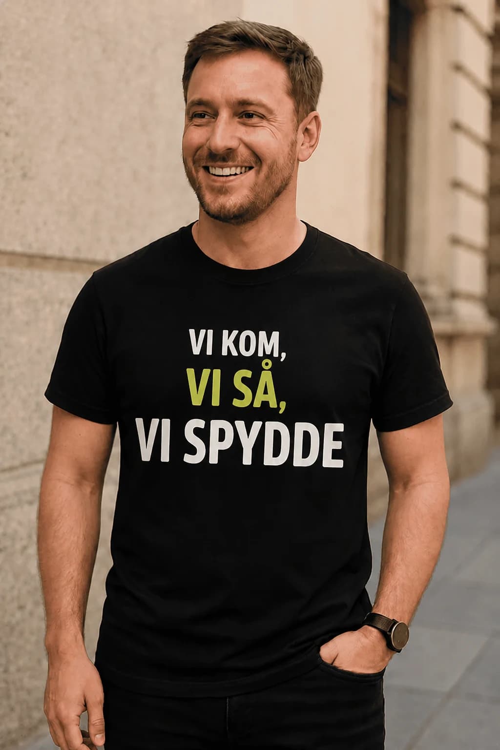 Smilende mann i svart morsom t-skjorte med festteksten «Vi kom, vi så, vi spydde» i hvit og limegrønn skrift
