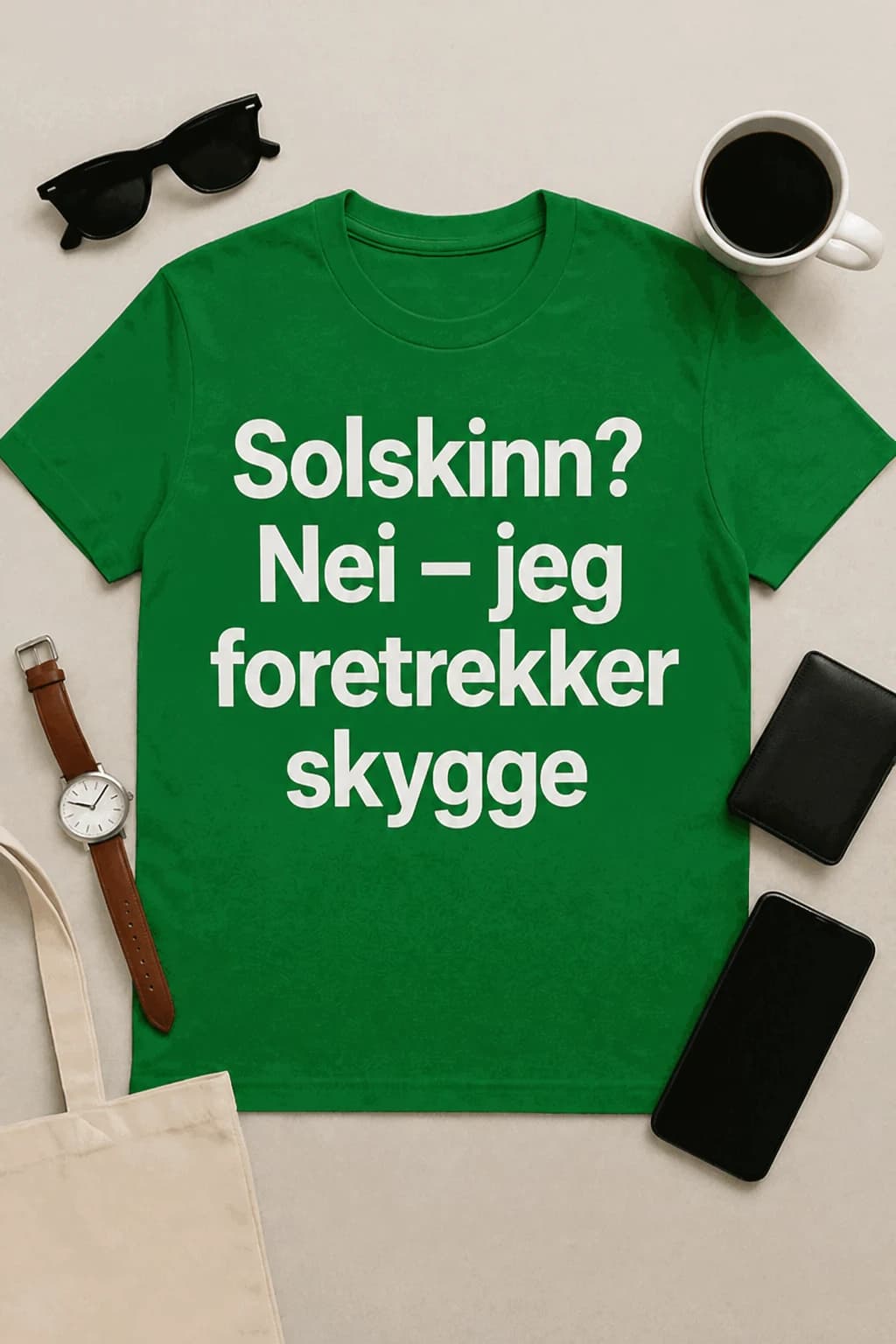 Grønn morsom t-skjorte med hvit tekst «Solskinn? Nei – jeg foretrekker skygge» lagt flatt ved solbriller