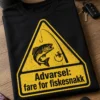 Sort og gul fiskeskjorte med advarselstriangler, fisk og fiskestang samt teksten Advarsel: fare for fiskesnakk