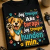 T-skjorte med teksten «Jeg trenger ikke terapi – jeg trenger hunden min.» og en glad, tegneserieaktig hund med løftet pote og små poteavtrykk.