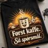 Kaffet-skjorte med en dampende kaffekopp, soloppgangsstråler og teksten «Først kaffe. Så spørsmål.»